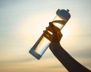 Human Hand Holds A Water Bottle Against The Setting Sun. UV-resistant plastic