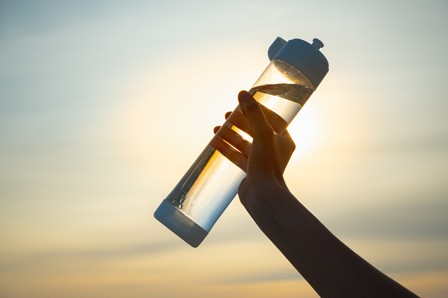 Human Hand Holds A Water Bottle Against The Setting Sun. UV-resistant plastic